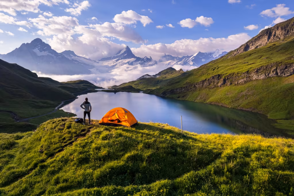 Wanderer neben einem orangen Zelt über einem Bergsee